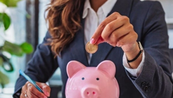 Businesswoman with piggy bank on desk (Adobe AI)